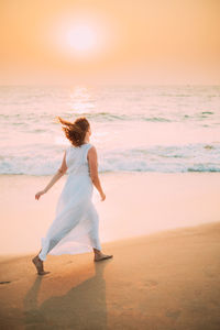 Rear view of woman standing at beach during sunset