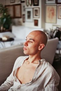 Thoughtful bald young man looking away while sitting at home