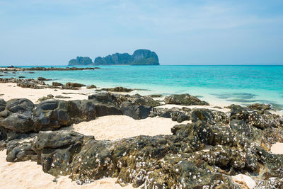 Tropical sea landscape with rocks at sand beach and rocky island at horizon