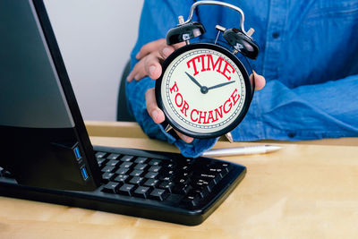 Midsection of man holding clock by computer at table