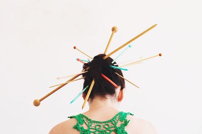 Rear view of woman wearing knitting needles against white background