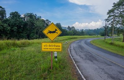 Road sign by trees against sky