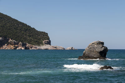 Rock formations in sea against clear blue sky