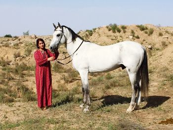 Portrait of young woman standing with horse on field