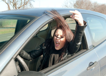 Portrait of young woman in car showing obscene gesture