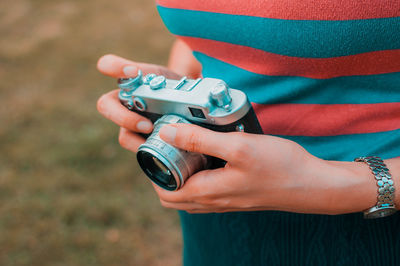 Midsection of woman holding camera while standing outdoors