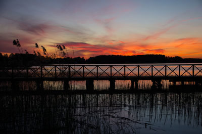 Silhouette bridge over river against sky during sunset