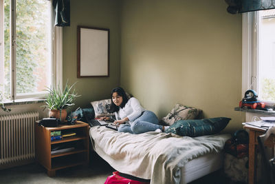 Full length of teenager using technology while lying on bed at home