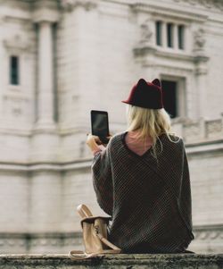 Rear view of woman photographing building with mobile phone