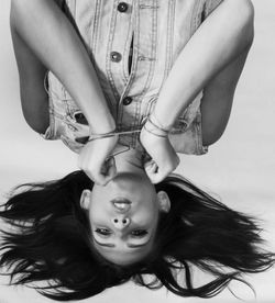 Close-up portrait of upside down woman with tied hands against white background