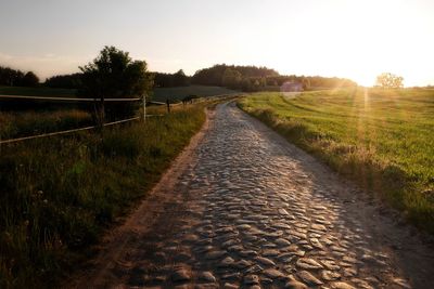 Dirt road amidst field against clear sky during sunset