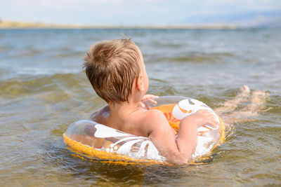 Shirtless boy with inflatable ring swimming in sea