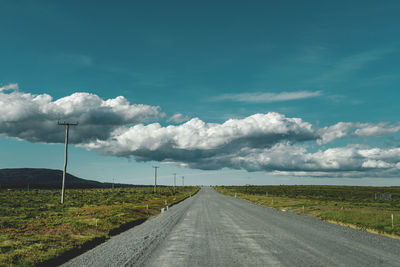 Empty road amidst field against sky