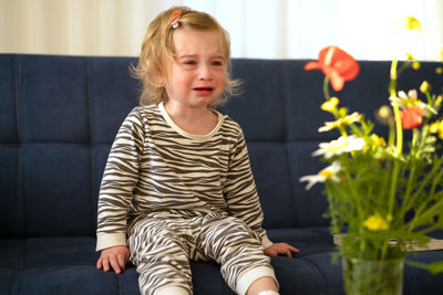 Cute girl crying while sitting on sofa at home