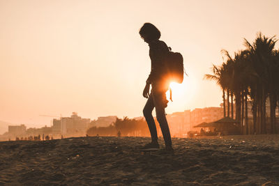 Silhouette woman walking at beach against clear sky during sunset