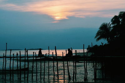 Silhouette people by swimming pool against sky during sunset