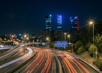 Light trails on road by illuminated buildings in city at night