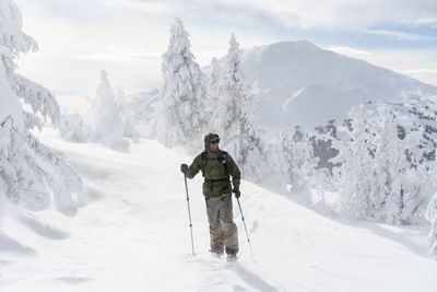 Full length of man with ski equipment standing on snowcapped mountain during foggy weather