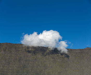 Smoke emitting from volcanic landscape against blue sky