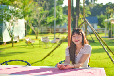 Young woman using mobile phone while sitting on swing at park