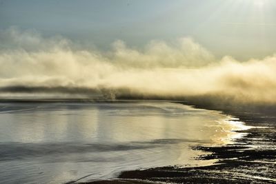 Scenic view of beach against cloudy sky during sunny day