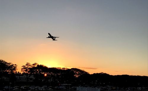 Silhouette airplane flying against sky during sunset