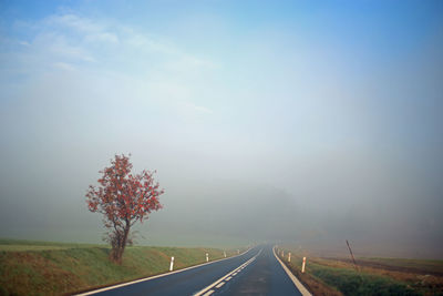 Country road amidst field against sky during foggy weather