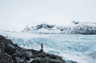 Rear view of man standing on snow covered mountain against sky