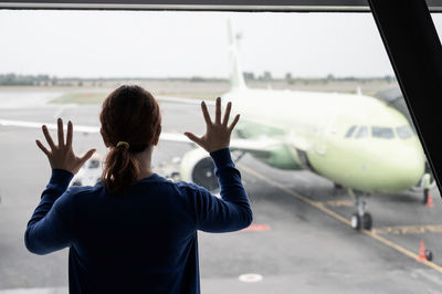 Rear view of woman looking at airplane through glass