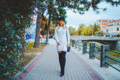 Portrait of young woman standing on footpath amidst trees