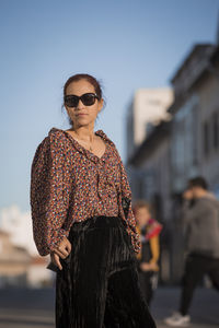 Portrait of woman wearing sunglasses while standing against city