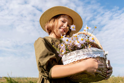 Girl in linen dress and a straw hat stands with a basket of daisies.  wellness and freedom concept.