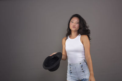 Portrait of young woman standing against gray background