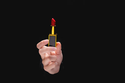 Close-up of hand holding cigarette against black background