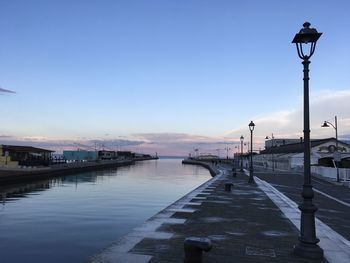 Street lights by canal against clear sky at sunset