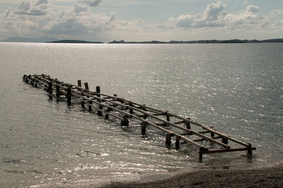 Wooden posts in sea against sky