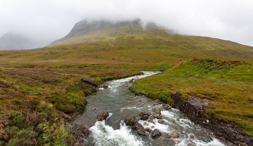 Scenic view of stream by mountains against sky