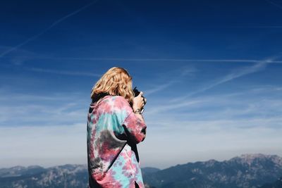 Rear view of woman photographing against blue sky