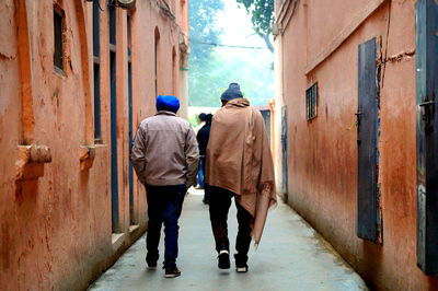 Rear view of men walking amidst buildings in city during winter