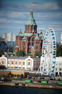 View of ferris wheel in city against cloudy sky