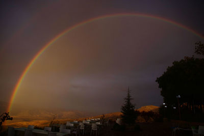 Rainbow over buildings in city against sky at sunset