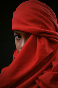 Portrait of boy covering face with red textile against black background