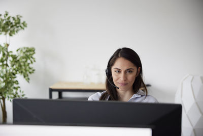 Smiling mid adult businesswoman using headset in office in front of computer screen