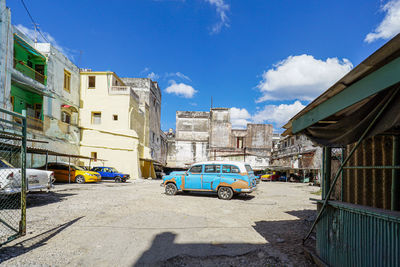 Cars on road by buildings against blue sky