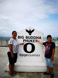 Portrait of mother and son pointing at sign against cloudy sky