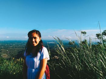 Portrait of young woman standing against blue sky