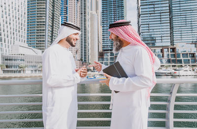 Business people discussing while standing against river in city