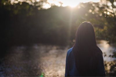 Rear view of woman standing at riverbank during sunset