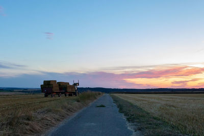 Road amidst field against sky during sunset