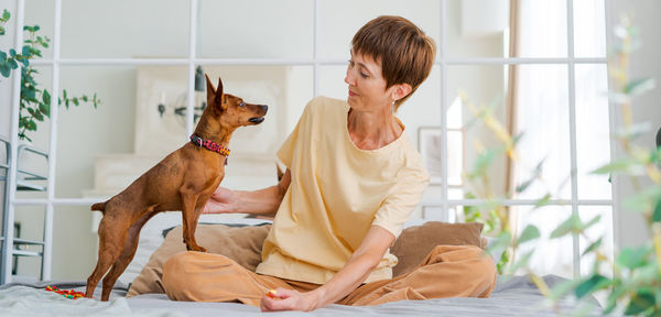 Owner playing with joyful dog at home, happy mature woman enjoying exercise